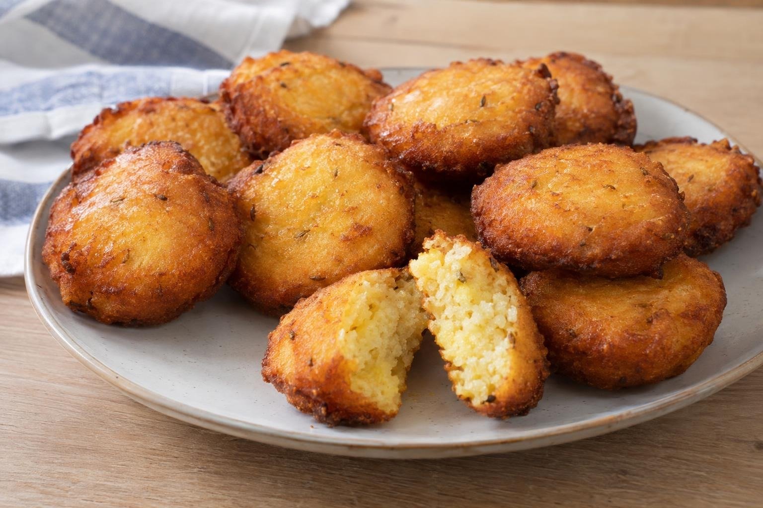 Arepitas de maíz dominicanas pequeñas y doradas, una de ellas partida para mostrar su interior tierno, servidas en un plato claro.