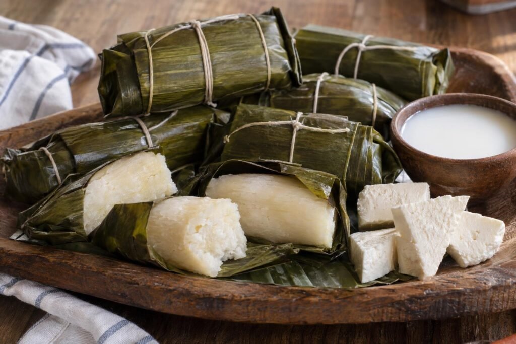 Bollos de yuca colombianos suaves y compactos, envueltos en hojas de plátano y servidos con queso costeño.