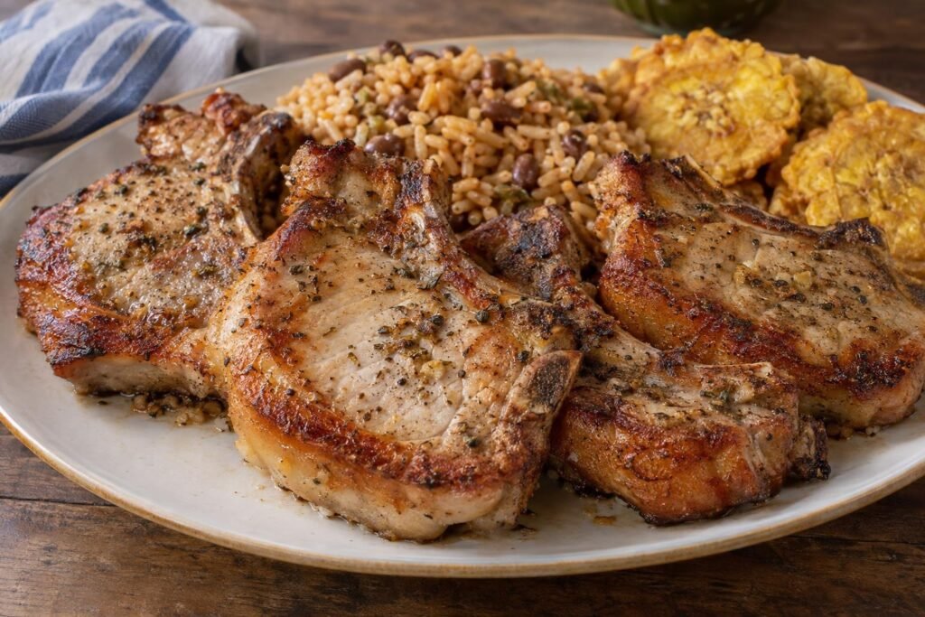 Chuletas can-can puertorriqueñas con piel y hueso, doradas y servidas con arroz con gandules y tostones