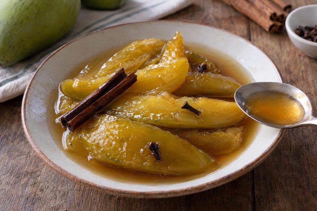 Tajadas de mango verde costeño cocidas en almíbar dorado con canela, servidas en un plato pequeño.