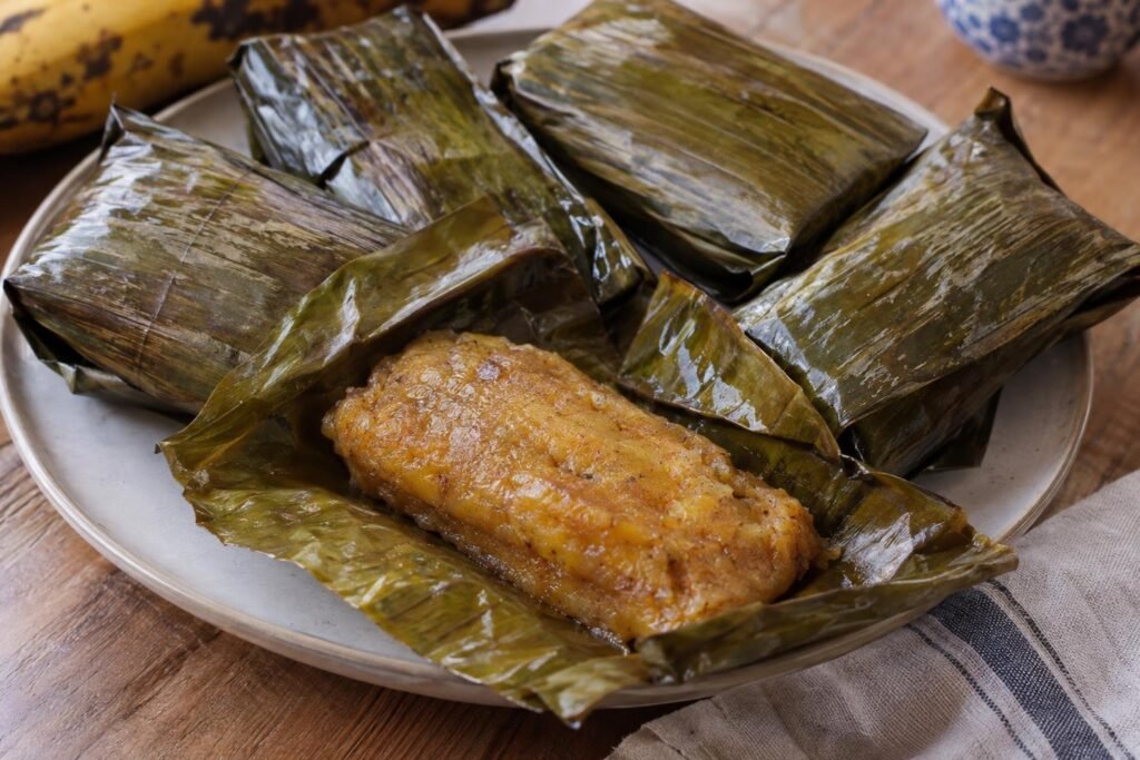 Envuelto de plátano maduro tolimense cocido al vapor, abierto sobre hojas de plátano y con masa dorada y tierna.