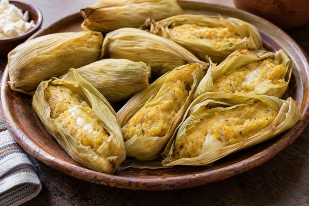 Humintas bolivianas de maíz fresco y queso horneadas dentro de hojas de choclo, servidas calientes en una fuente.