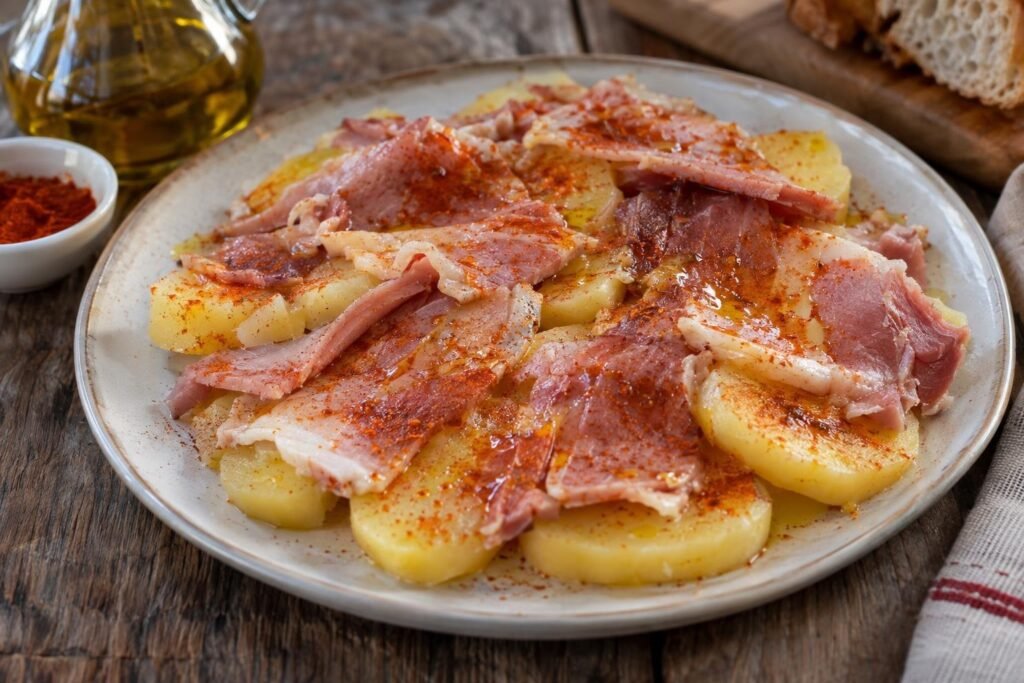 Fuente de lacón cocido sobre rodajas de patata con aceite de oliva y pimentón rojo.