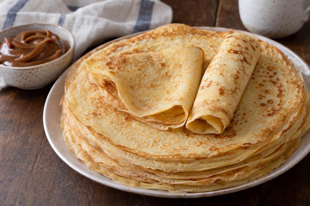 Pila de panqueques argentinos finos y dorados con dulce de leche al lado