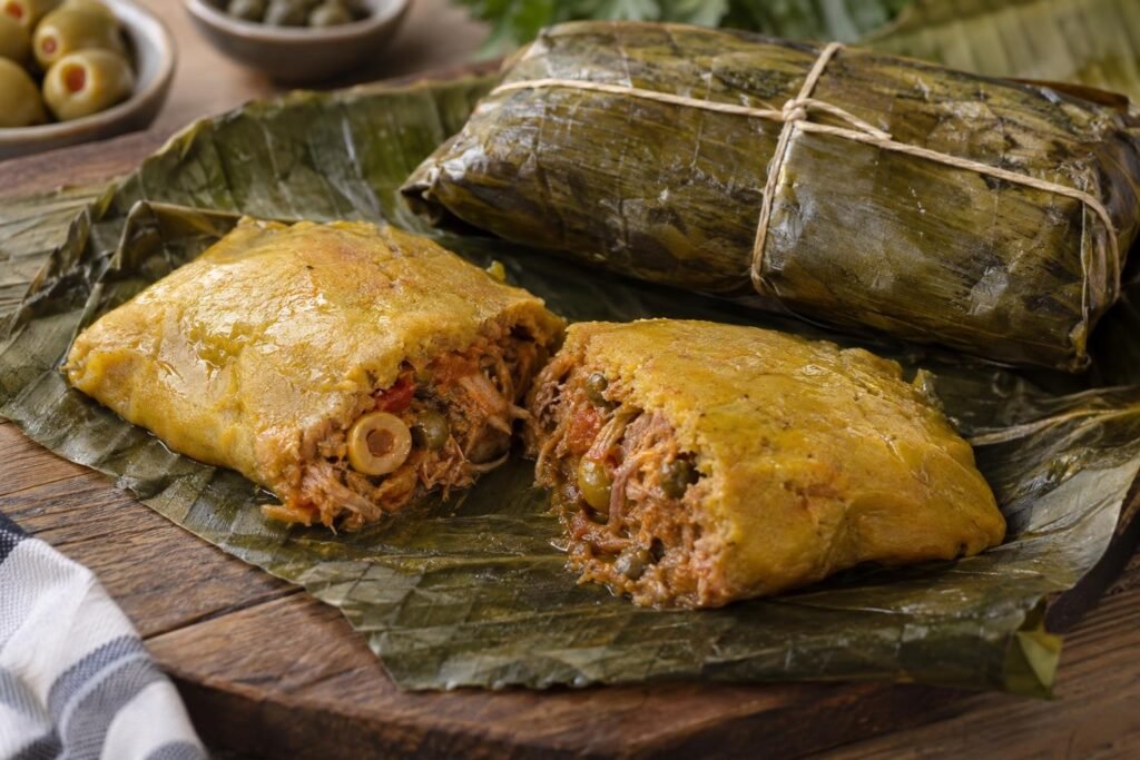 Pasteles puertorriqueños de masa cocidos, uno abierto con relleno de cerdo y masa de plátano verde, y otro envuelto en hoja de plátano.