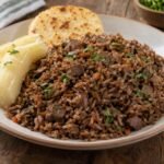 Porción de pepitoria santandereana con arroz oscuro, vísceras de cabro picadas y cilantro, acompañada de yuca y arepa.