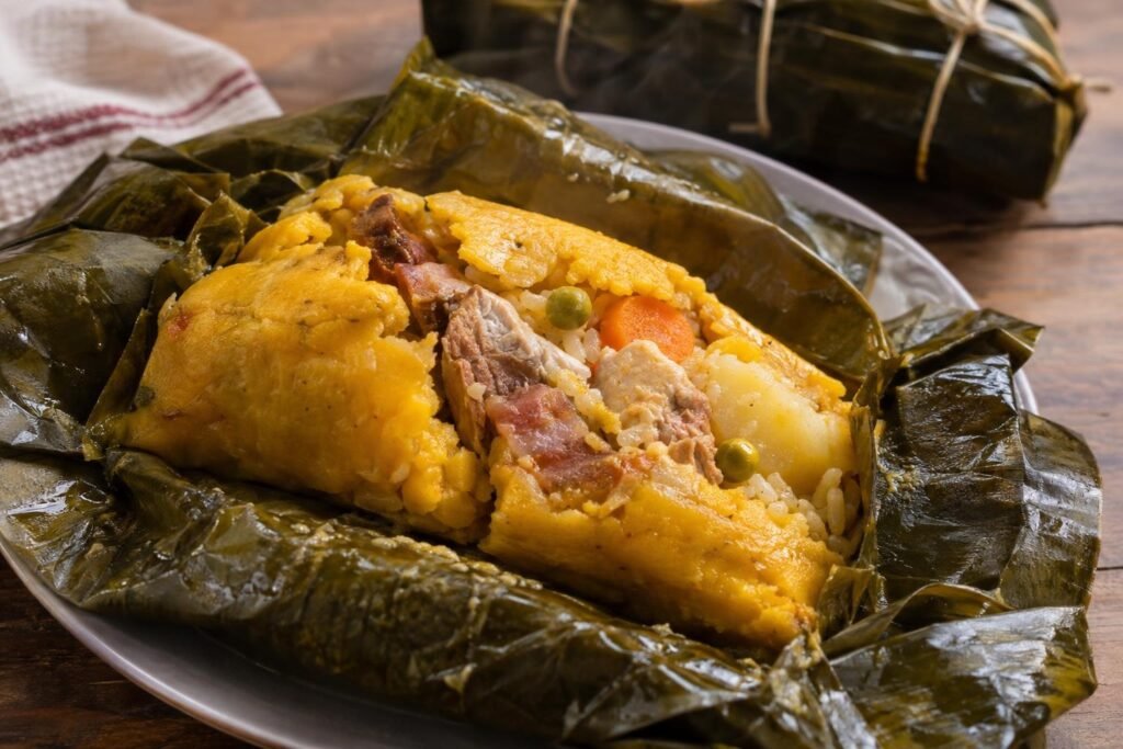 Tamal tolimense abierto sobre hoja de plátano, con masa amarilla, cerdo, pollo, arroz, papa, zanahoria y arvejas.