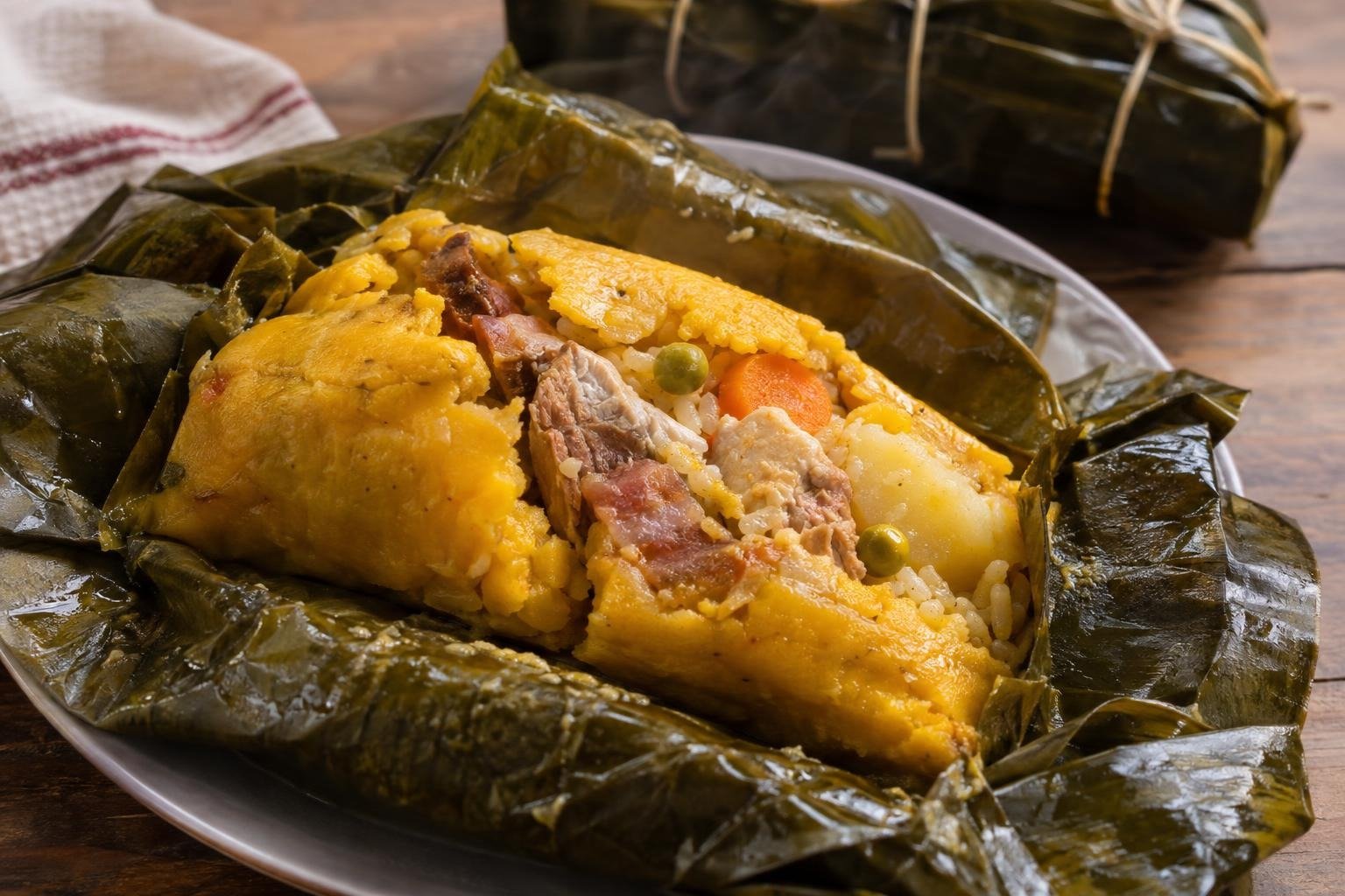 Tamal tolimense abierto sobre hoja de plátano, con masa amarilla, cerdo, pollo, arroz, papa, zanahoria y arvejas.