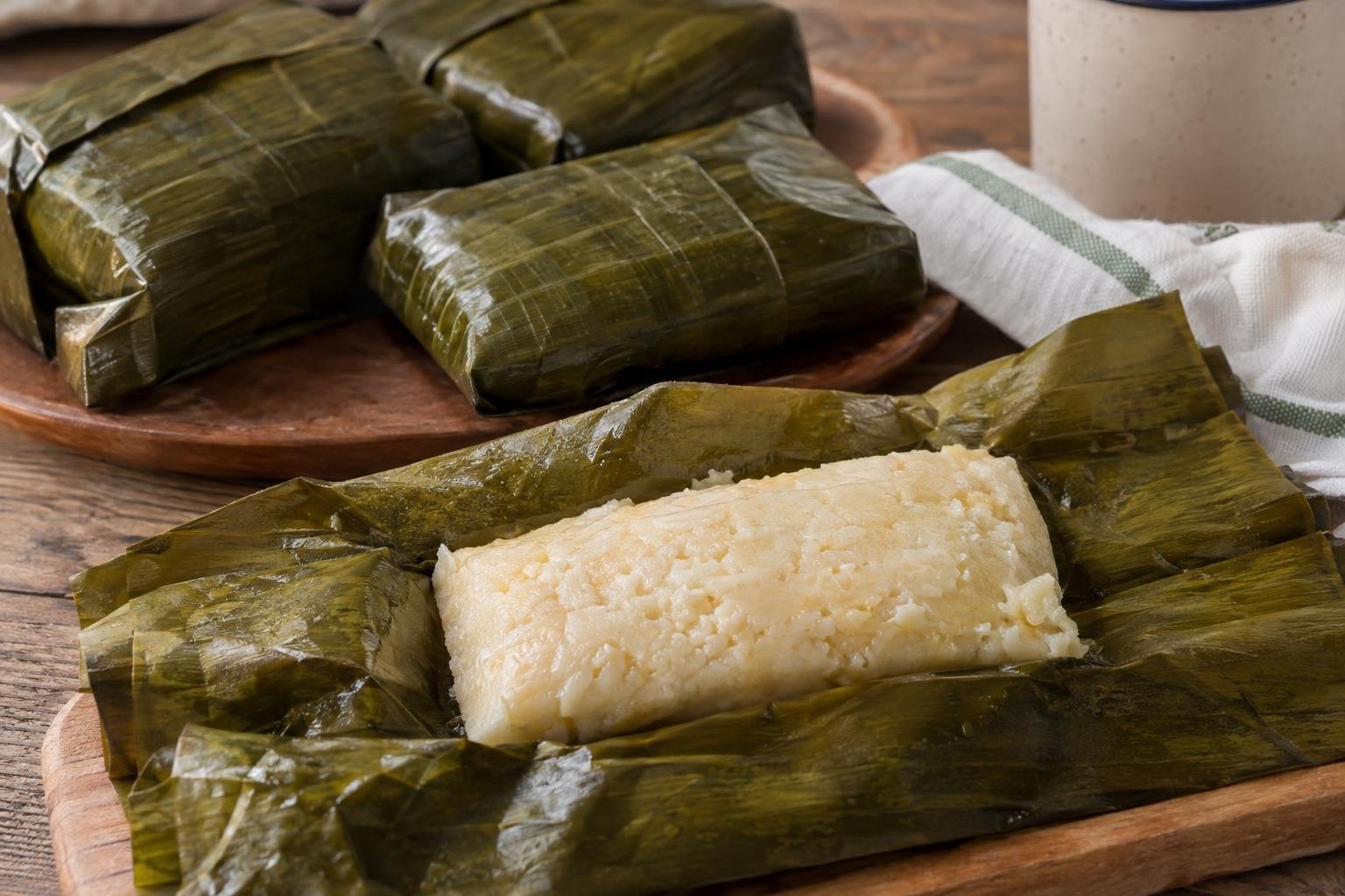 Tungos llaneros de arroz y cuajada cocidos al vapor, envueltos en hojas y uno abierto para mostrar su interior suave y compacto.